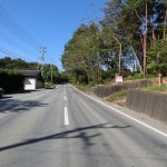 物件西側県道の南側から北方向を撮影。物件は道路右側。